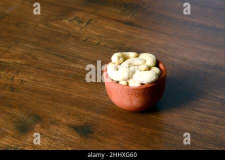 Arachide crude arrosto salate in una ciotola di legno su un tavolo rustico, sano spuntino vegetariano, anacardium occidentale, anachide su sfondo bianco, anachide. Foto Stock