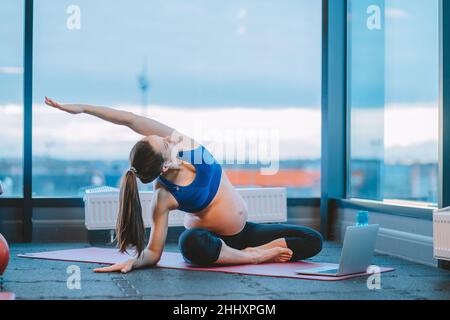 la donna incinta fa le esercitazioni di yoga con il laptop in palestra o a casa Foto Stock