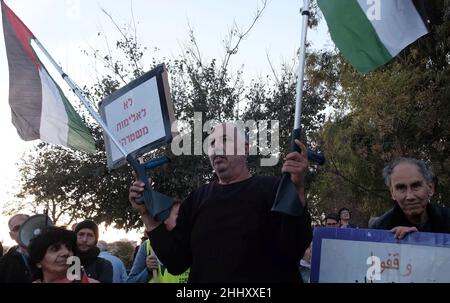 Il palestinese Muhammad abu Hummus tiene le sue stampelle con la bandiera palestinese, mentre gli attivisti di sinistra israeliani e i palestinesi hanno gridato slogan durante una manifestazione contro l'occupazione israeliana e l'attività di insediamento nel quartiere di Sheikh Jarrah il 10 dicembre 2021 a Gerusalemme, Israele. Il quartiere palestinese di Sheikh Jarrah è attualmente il centro di una serie di controversie di proprietà tra palestinesi e israeliani ebrei di destra. Alcune case sono state occupate dai coloni israeliani a seguito di una sentenza della Corte. Foto Stock