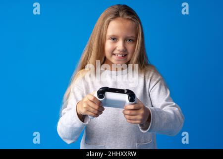 Giovane ragazza cute gioca gioco di computer con joystick su sfondo blu Foto Stock