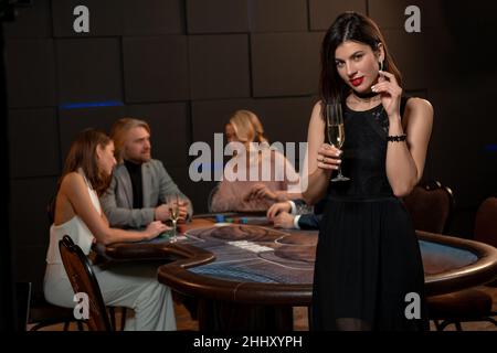 Giovane bruna che solleva bicchiere di champagne per il gioco di poker di successo nel casinò Foto Stock