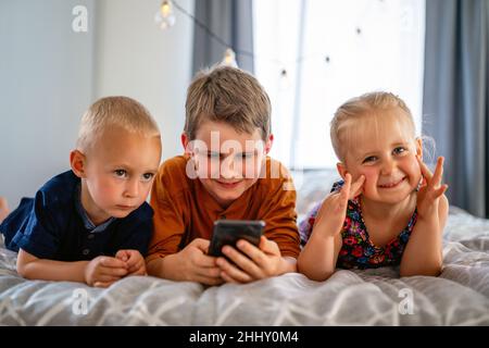 Concetto di smartphone per bambini con tecnologia infantile. Bambini piccoli felici che giocano sul telefono cellulare Foto Stock