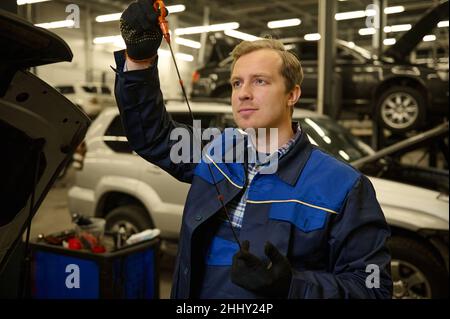 Auto riparatore meccanico di controllare il livello di olio nel motore di auto, sotto il cofano del veicolo service shop Foto Stock