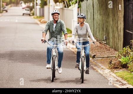 È stata una buona idea. Shot di una coppia allegra senior che pedalano insieme in bicicletta all'esterno di un sobborgo. Foto Stock
