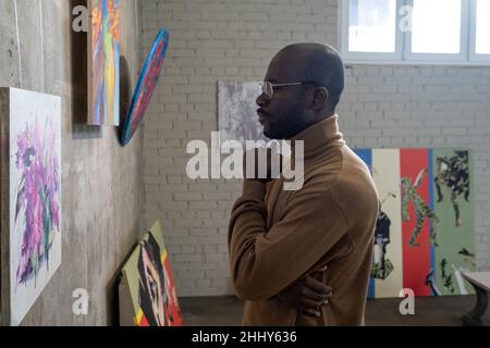 Uomo africano serio guardando bei dipinti mentre si erge in galleria d'arte Foto Stock