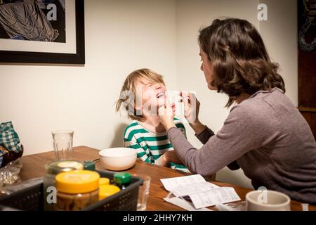 Un giovane ragazzo si lamenta mentre sua madre esegue un rapido test antigenico covid19 inserendo un bastoncino nel naso al tavolo della colazione prima della scuola, ad Amsterdam, nei Paesi Bassi. Foto Stock