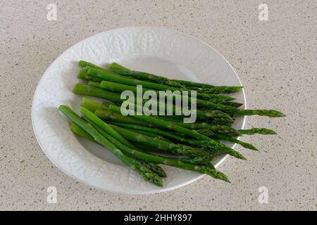 Asparagi - deliziose, fresche, teneri, lance di asparagi verdi - su un piatto bianco - sfondo beige Foto Stock
