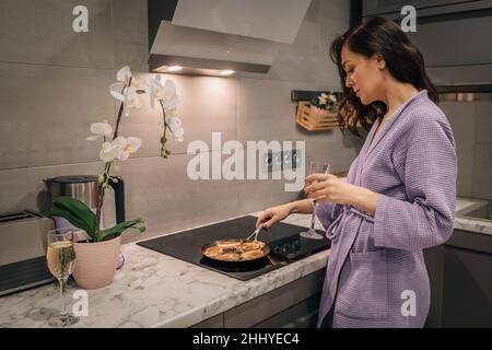 Le giovani donne in cucina si preparano frittelle fritte, dolci in padella sul piano di cottura. Concetto di stile di vita di cucina a casa. Foto Stock