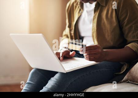 Viziatevi, lo meritate. Scatto ritagliato di un uomo irriconoscibile utilizzando un computer portatile e una carta di credito per fare acquisti online mentre si siede sul suo divano a. Foto Stock