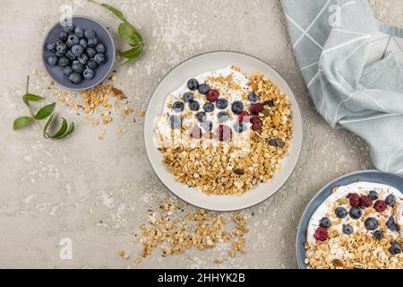 yogurt con muesli fatti in casa e lamponi e mirtilli in un piatto su sfondo grigio di cemento. vista dall'alto. colazione deliziosa e salutare Foto Stock