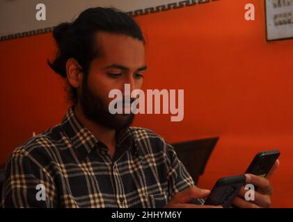 Primo piano vista laterale di un bel bearded uomo con capelli bun, tenendo due telefoni - Stock Photo Foto Stock
