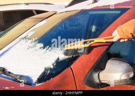 Rimuovere la neve dalla modalità automatica. Spazzola in mano mans. L'uomo libera l'auto arancione dalla neve. Parabrezza dell'auto. Foto Stock