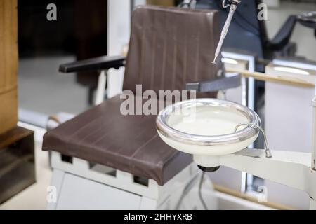 Un vecchio lavandino dentale sovietico contro una poltrona marrone. Odontoiatria dei tempi dell'URSS. Messa a fuoco soft Foto Stock