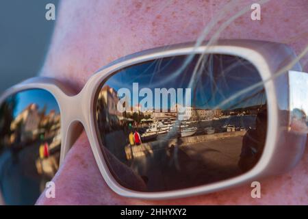 Occhiali da sole negli occhi di una donna e nel riflesso dei bicchieri possono vedere la città sull'Adriatico sull'isola di Hvar. Foto Stock