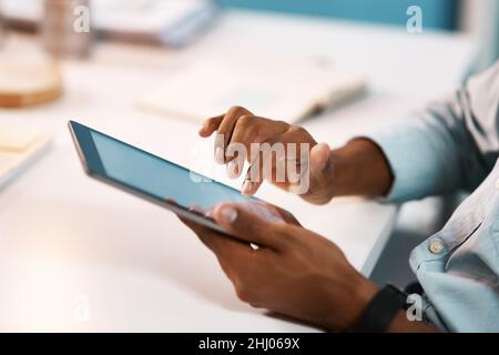 Connettersi al mondo aziendale. Scatto di un uomo d'affari irriconoscibile che usa un tablet digitale mentre lavora tardi nel suo ufficio. Foto Stock