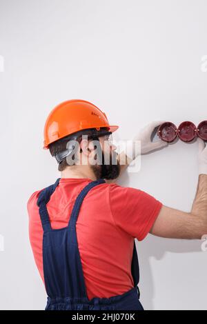 l'elettricista nel casco installa le prese Foto Stock