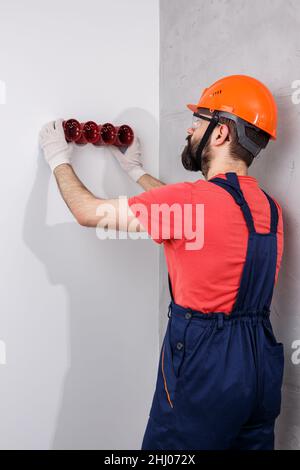 l'elettricista nel casco installa le prese Foto Stock