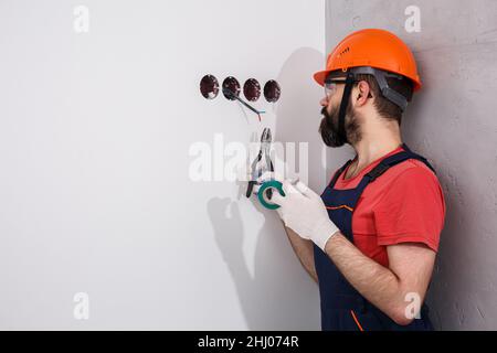 l'elettricista nel casco installa le prese Foto Stock