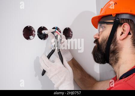 l'elettricista nel casco installa le prese Foto Stock