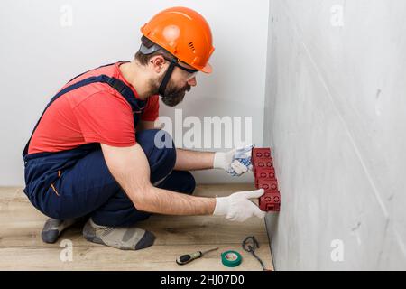 l'elettricista nel casco installa le prese Foto Stock