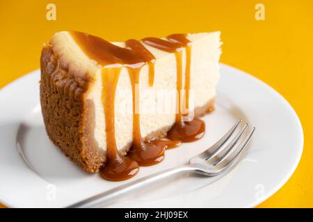 Fetta di cheesecake con aggiunta di caramello sul piatto bianco, vista closeup Foto Stock