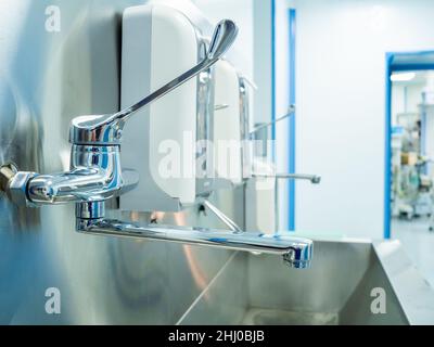 Stazione di lavaggio chirurgia ospedaliera per la disinfezione dei medici prima dell'intervento chirurgico. Lavaggio a mano in un ospedale. Messa a fuoco selettiva. Rubinetti e lavabo per chirurghi in acciaio inox. Foto Stock