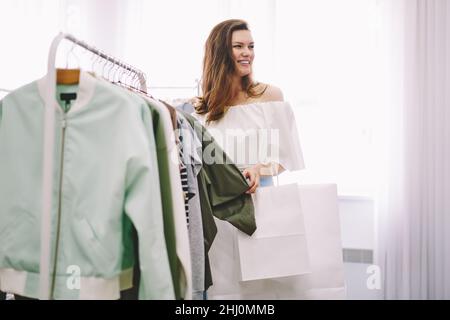 Donna sorridente che sceglie la giacca in negozio Foto Stock