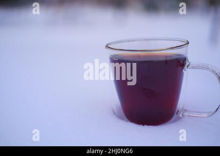 Tè al teacup in vetro a doppia parete su una scrivania innevata in inverno all'aperto Foto Stock