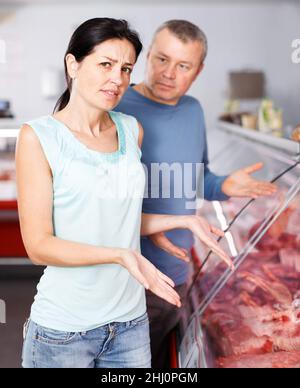 Triste coppia di clienti adulti che scelgono la carne in negozio Foto Stock