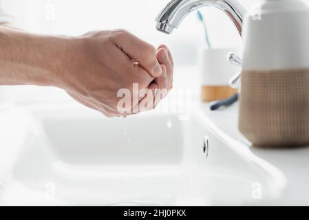 vista ravvicinata delle mani maschili vicino al rubinetto e articoli da bagno sfocati Foto Stock