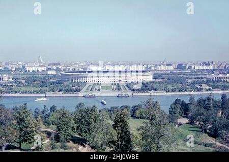 Una fotografia del 1960s dello stadio Luzhniki e dei suoi dintorni, situato vicino al fiume Moskva, Mosca, Russia. Il nome completo del ‘Stadio Nazionale’ è ‘Grand Sports Arena del complesso Olimpico di Luzhniki’. La sua capacità totale di 81.000 posti a sedere, il più grande stadio di calcio della Russia. Lo stadio fu costruito nel 1955-56 come Grand Arena del Central Lenin Stadium. Lo stadio originale fu demolito nel 2013 per fare posto ad un nuovo stadio. Tuttavia, il tetto autoportante (costruito nel in1996) e la parete originale della facciata sono stati conservati – una fotografia d'epoca 1960s da una trasparenza amatoriale del colore. Foto Stock