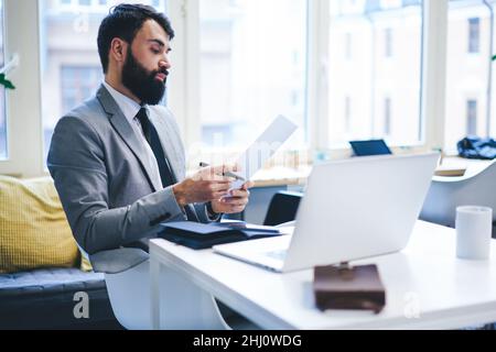 Uomo d'affari concentrato che guarda attraverso i documenti in ufficio Foto Stock