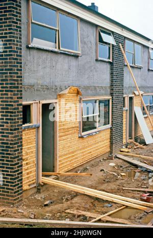 Moderna costruzione di case a Stevenage New Town, Hertfordshire, Inghilterra, Regno Unito nel 1963. Qui, sui fronti di una terrazza di case, l'isolamento (sottile secondo gli standard moderni) è tenuto in atto da legno che ingrasso prima di uno strato di finitura di piastrelle appese - vedere Alamy 2HJ0WDC per i lavoratori che applicano la piastrella. Stevenage si trova a circa 30 miglia (50 km) a nord di Londra. Nel 1946 Stevenage è stata designata la prima New Town del Regno Unito in base al New Towns Act. Questa immagine proviene da una vecchia trasparenza del colore amatoriale – una fotografia d'epoca del 1960s. Foto Stock