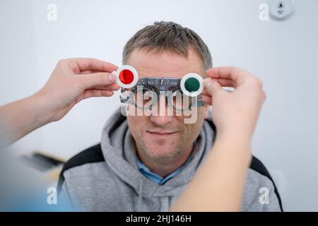 Correzione della visione. Selezione di occhiali. Gli studi professionali si montano sul viso del paziente maschile mentre il medico controlla la vista nell'oftalmologo moderno Foto Stock