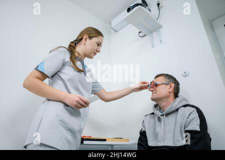 Correzione della visione. Selezione di occhiali. Gli studi professionali si montano sul viso del paziente maschile mentre il medico controlla la vista nell'oftalmologo moderno Foto Stock
