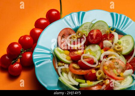 Goiania, Goias, Brasile – 25 gennaio 2021: Un piatto di verdure assortite su sfondo arancione e un mazzetto di pomodori maturi. Foto Stock