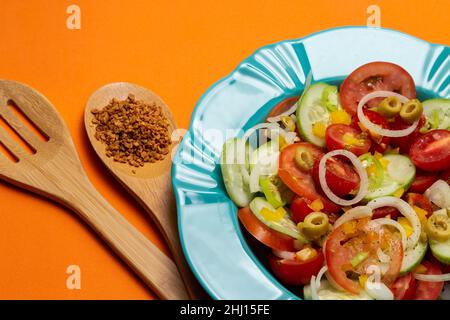 Goiania, Goias, Brasile – 25 gennaio 2021: Un piatto con insalata di verdure e due posate di legno su sfondo arancione. Foto Stock