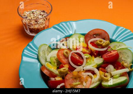 Goiania, Goias, Brasile – 25 gennaio 2021: Un piatto di insalata di verdure con fondo arancione e un bicchiere di condimento disidratato. Foto Stock