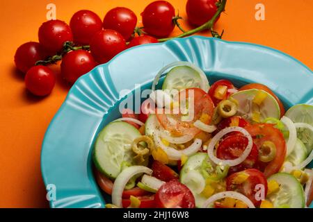 Goiania, Goias, Brasile – 25 gennaio 2021: Un piatto di verdure assortite su sfondo arancione e un mazzetto di pomodori maturi. Foto Stock