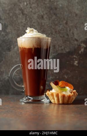 Bevanda a base di caffè con panna montata e torta di frutta su sfondo rustico. Foto Stock