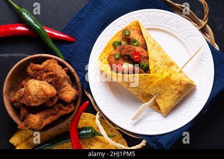 Concetto alimentare tortilla di pollo fritto piccante con peperoncini tritati su sfondo nero di pietra ardesia con spazio copia Foto Stock