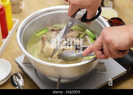 hot pot per zuppa di pollo intera coreana, tagliando il pollo intero con le forbici Foto Stock