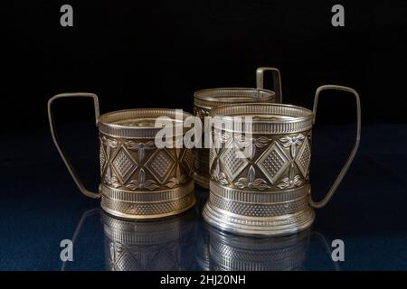 Un portabicchieri in metallo su un tavolo blu con un riflesso. Utensili da cucina su sfondo nero Foto Stock