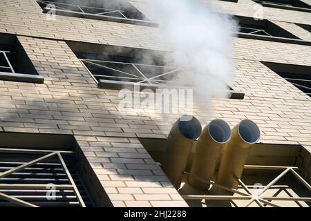 Uno scarico di vapore bianco da tre camino di un edificio di mattoni con le ombre del sole Foto Stock