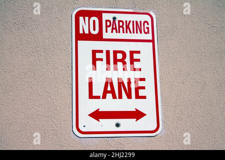 Non c'è parcheggio, vicolo dei vigili del fuoco bianco e rosso appeso su un muro di cemento sotto un forte sole estivo Foto Stock