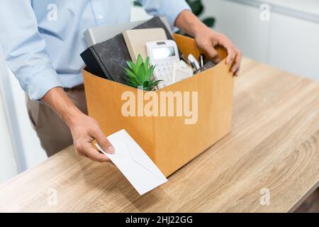 Concetto di dimissioni l'ufficiale maschio in piedi, mettendo la sua scatola di suo appartiene sulla scrivania e consegnando la lettera bianca a qualcuno. Foto Stock