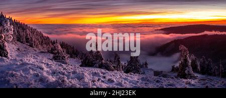 Paesaggio panoramico con alberi di abete rosso ricoperti di rime dopo il tramonto, vista da una gamma di moulatin alla valle piena di nebbia e nubi basse durante la temperatura Foto Stock