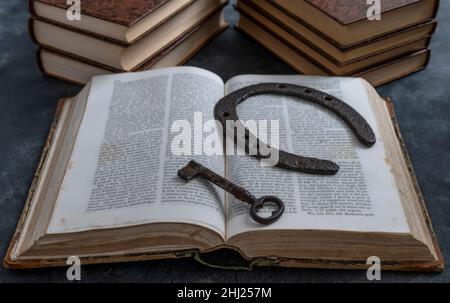 Una vecchia chiave e un vecchio ferro di cavallo riposano sulle pagine di un antico libro aperto, con altri libri sullo sfondo Foto Stock