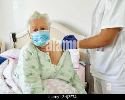 Anziano adulto anziano donna caucasica riceve il vaccino Covid-19 a casa dal medico Foto Stock