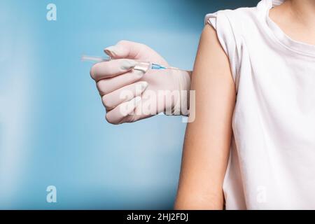 Mano del medico in guanti bianchi che fanno l'iniezione con la siringa, vicino su sfondo blu con spazio di copia. Foto Stock